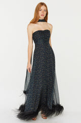 A model wears a strapless corseted chiffon long gown with a matching neck scarf. The dress has black feathers at the hem. The print is black, red, and green small flowers on a black base.