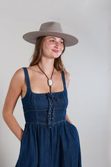 Woman wearing a Western-Ivory-Stone-Bolo-Tie, a Lace-Up-Corset-Midi-Dress-Dark-Denim and gray flat brim hat -Fleastyle