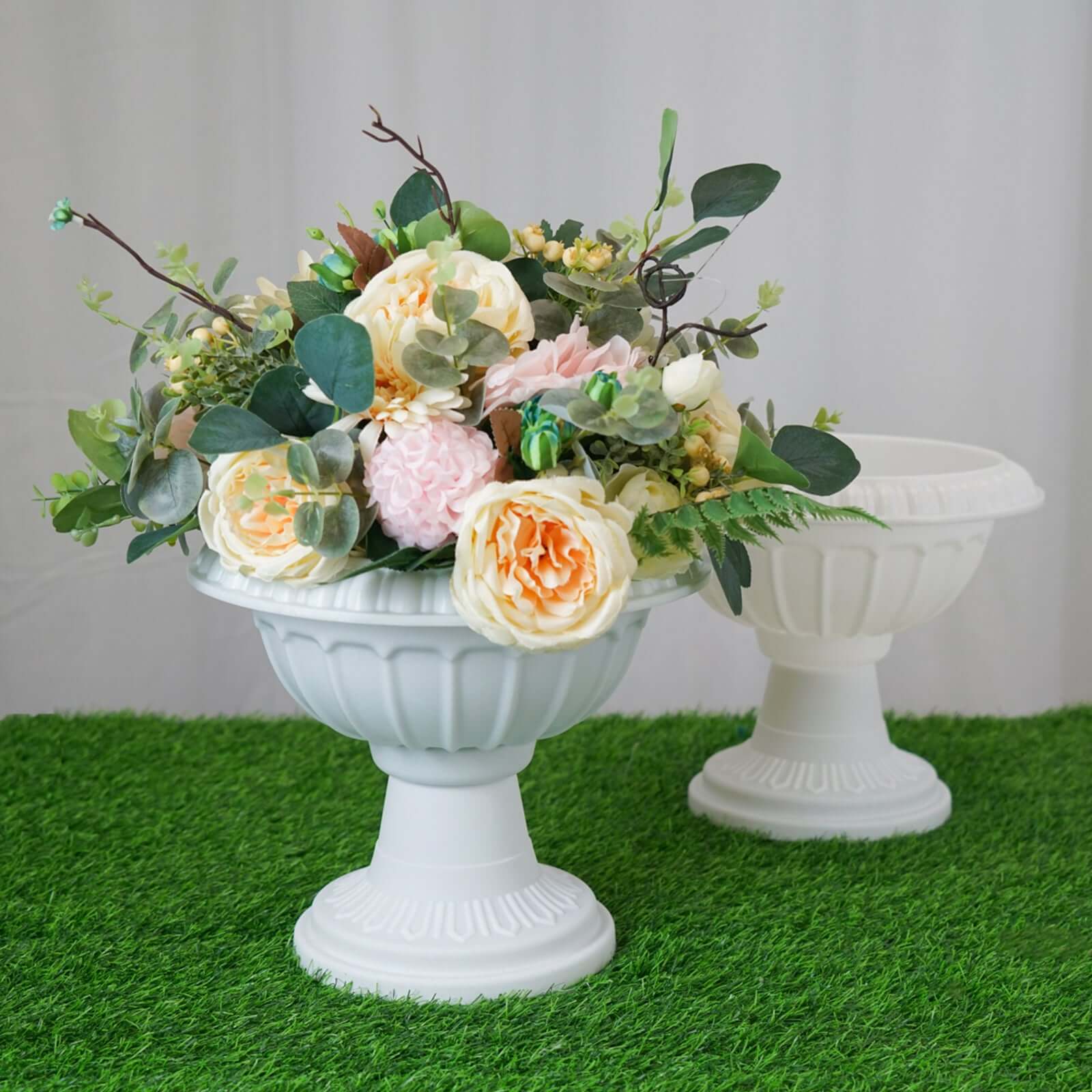 White urn with floral arrangement on grass backdrop.
