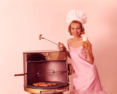 1960s Woman Wearing Pink Party Dress And Chef Hat Grilling Hot Dogs Drinking Beer