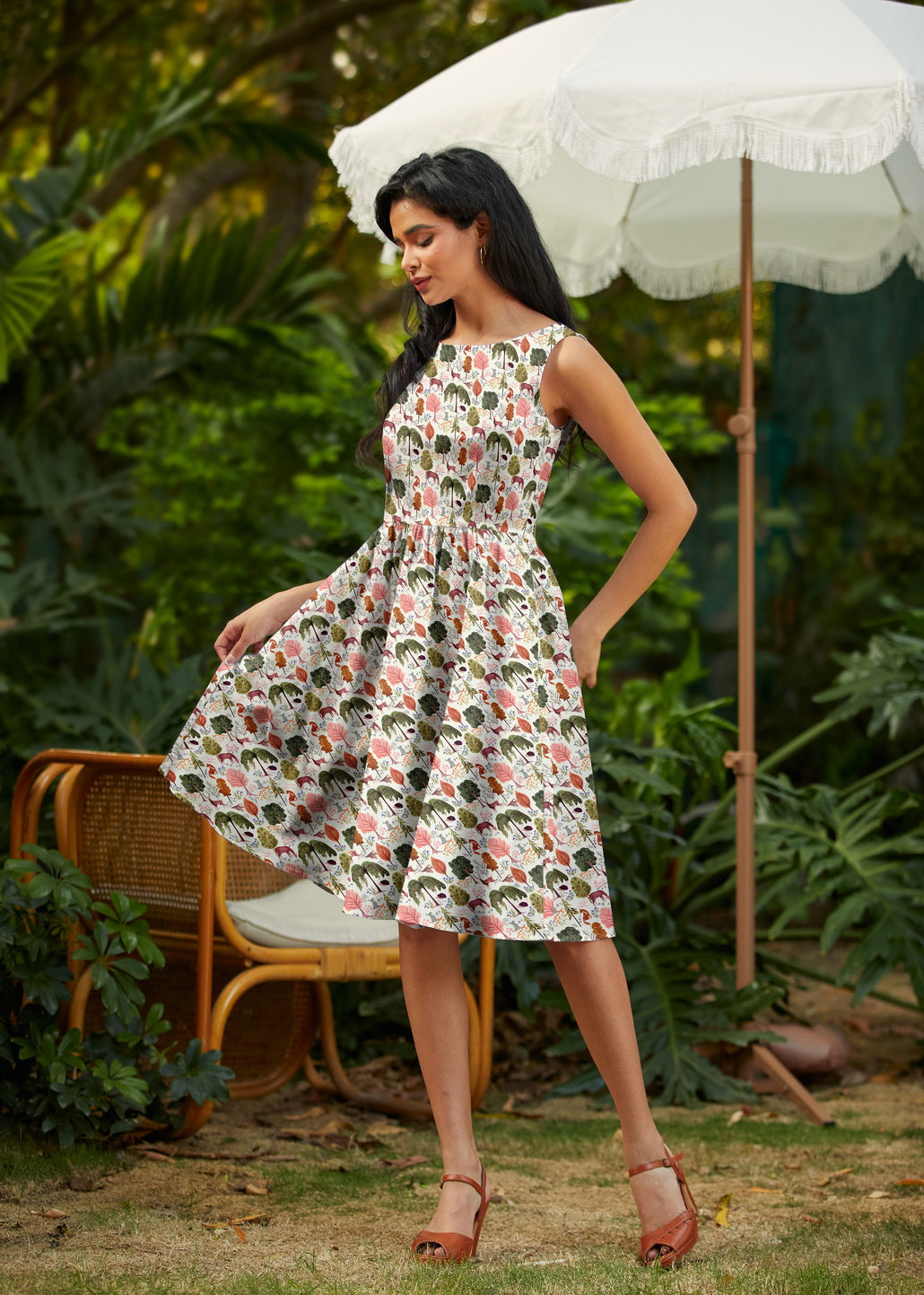 Woman in a floral dress standing outdoors with a white umbrella and chair in the background.