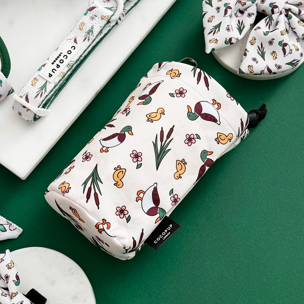 Cocopup London drawstring treat pouch in Puddle Pup pattern on green surface beside a dog collar.