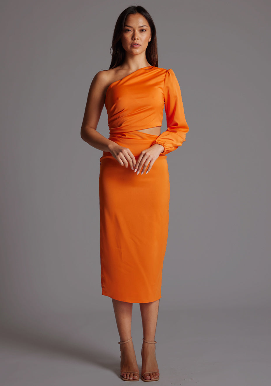 Front image of a model wearing an orange mid dress with a asymmetric, one long sleeve design and subtle side cut-out. The design featured is the Vesper Niccola Orange Midi Dress