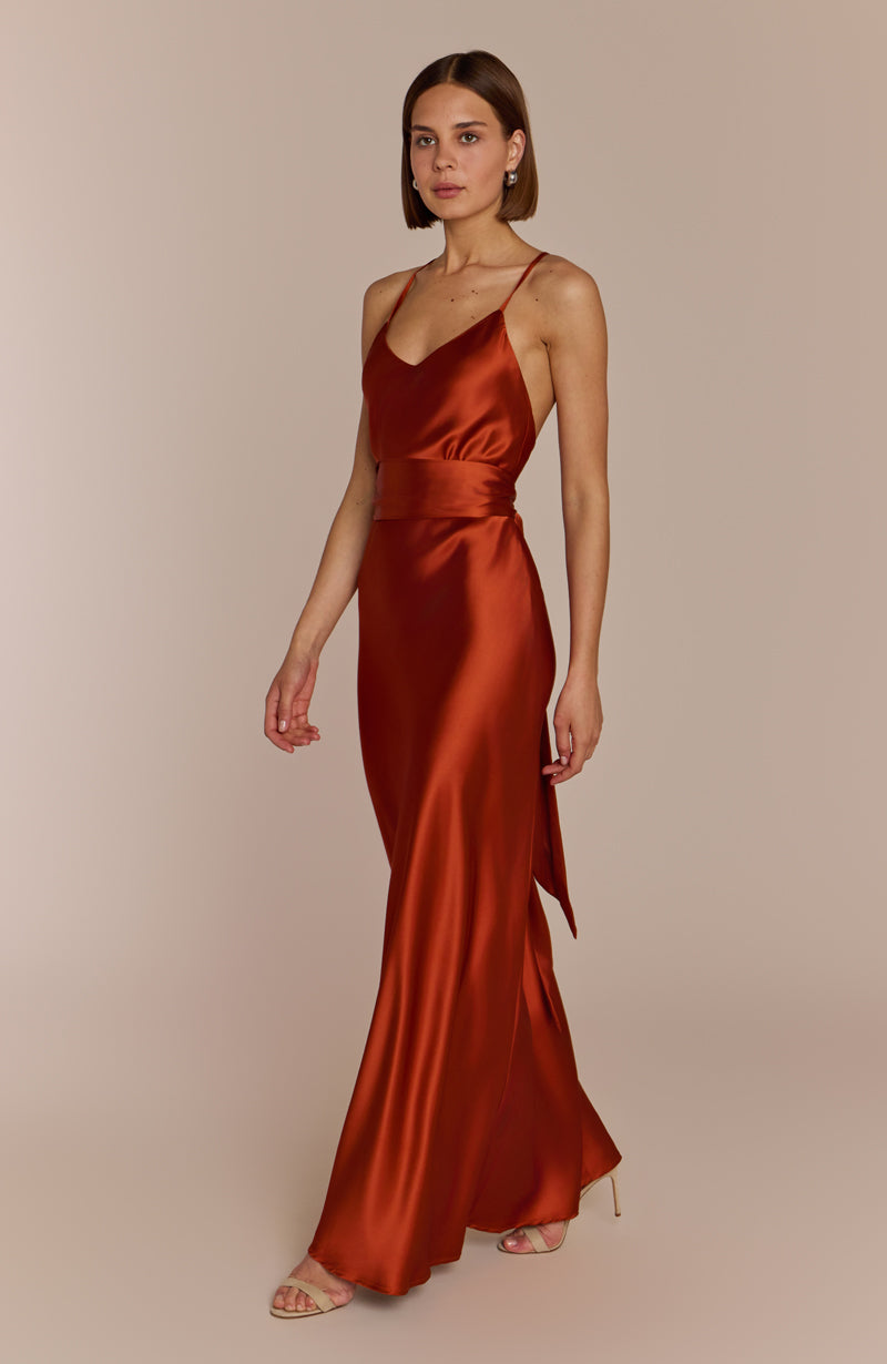 Woman wearing a rust-colored satin dress against a beige background