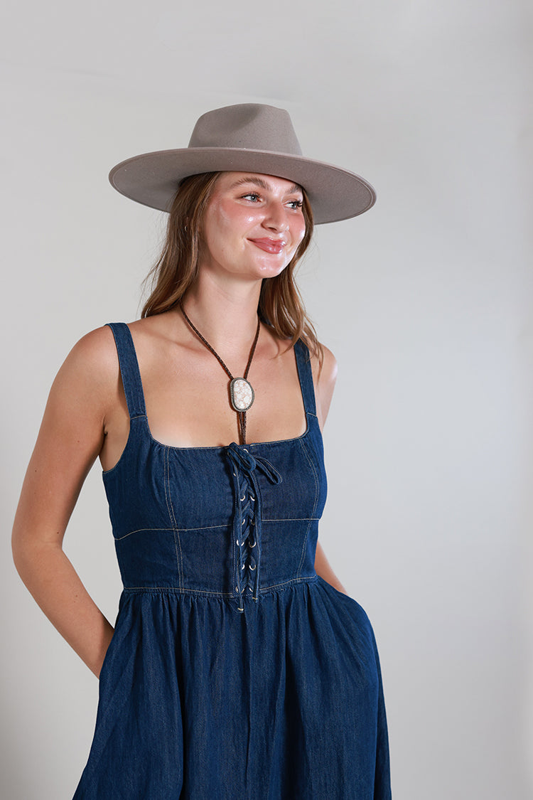 Woman wearing a Western-Ivory-Stone-Bolo-Tie, a Lace-Up-Corset-Midi-Dress-Dark-Denim and gray flat brim hat -Fleastyle