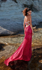 A woman stands on rocky terrain near water, wearing the Strappy Long Sequin Prom Dress: Aerie Couture 207—a bright pink gown with sequins, crisscross straps, backless design, and a flowing train.