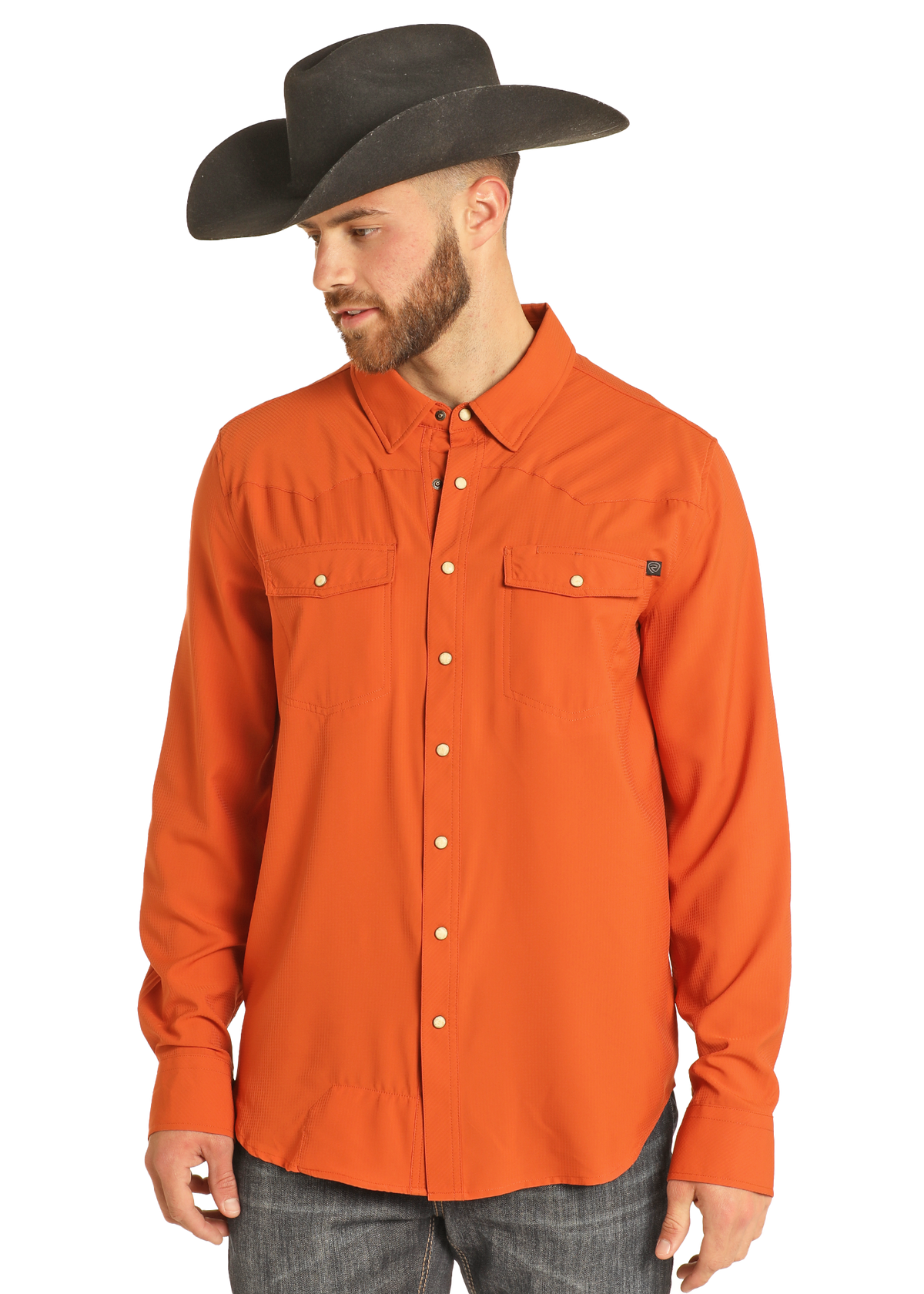 A man wears the Rock & Roll Denim TEK Western Burnt Orange Long Sleeve Shirt and a wide-brimmed black cowboy hat, looking down and to the side against a plain white background.