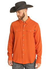 A man wears the Rock & Roll Denim TEK Western Burnt Orange Long Sleeve Shirt and a wide-brimmed black cowboy hat, looking down and to the side against a plain white background.