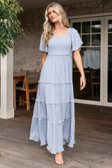 Front view of dusty blue Lenora smocked dotted maxi dress with square neckline, smocked bodice, and ruffle-tiered skirt flowing to ankle length.