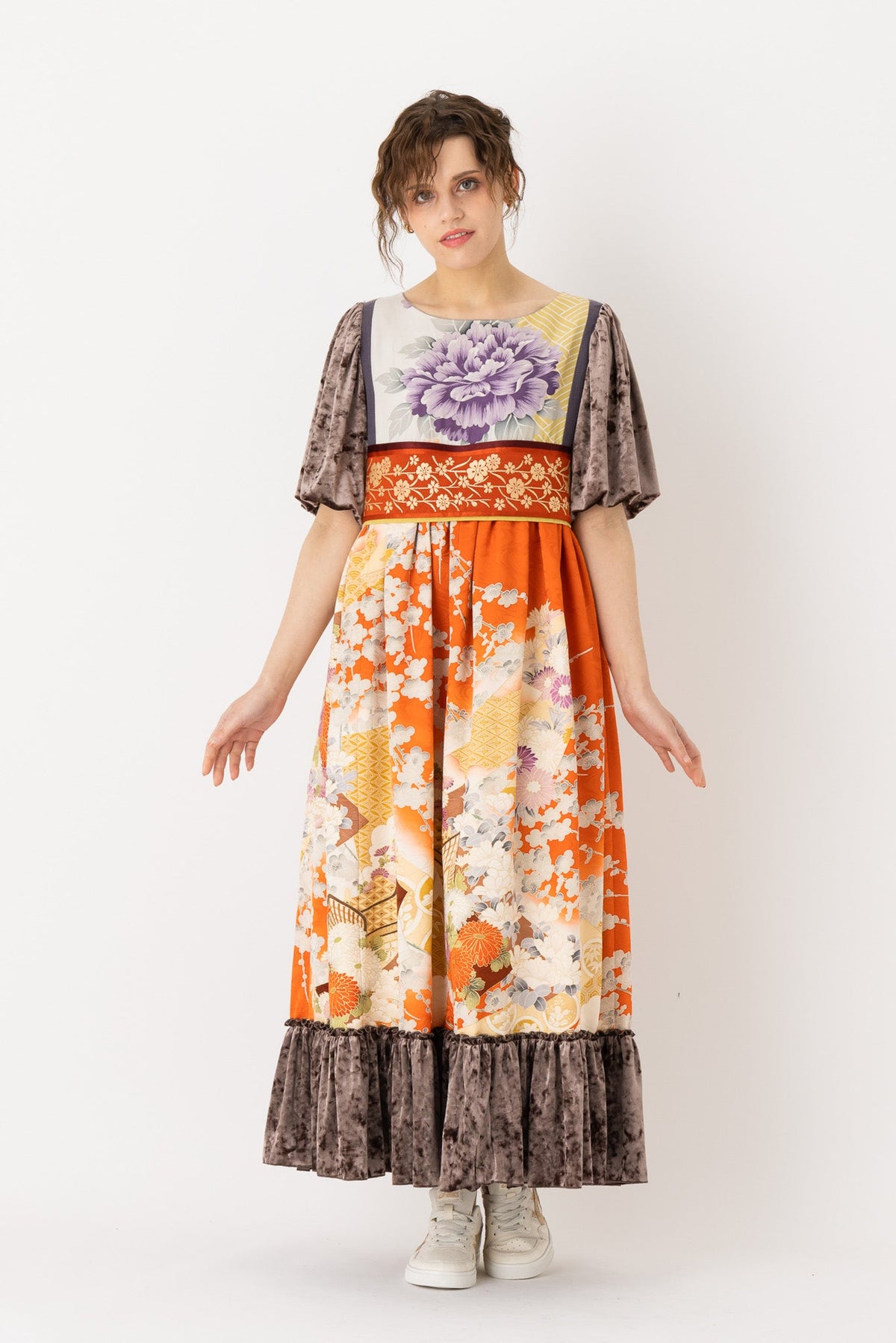 A woman is wearing an empire dress with a classic empire waist, showcasing an empire style dress. This empire waist dress is quite long, making it an example of a high waist maxi dress. This high waist dress enhances her figure. This maxi empire dress exudes sophistication and elegance making it ideal for a formal occasion or a leisurely evening out.