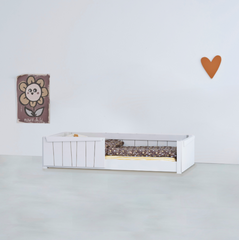 A white wooden toddler floor bed with partial vertical-slat safety rails, styled with floral bedding in a minimalist room.