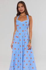 Woman wearing a blue dress with orange polka dots against a plain background
