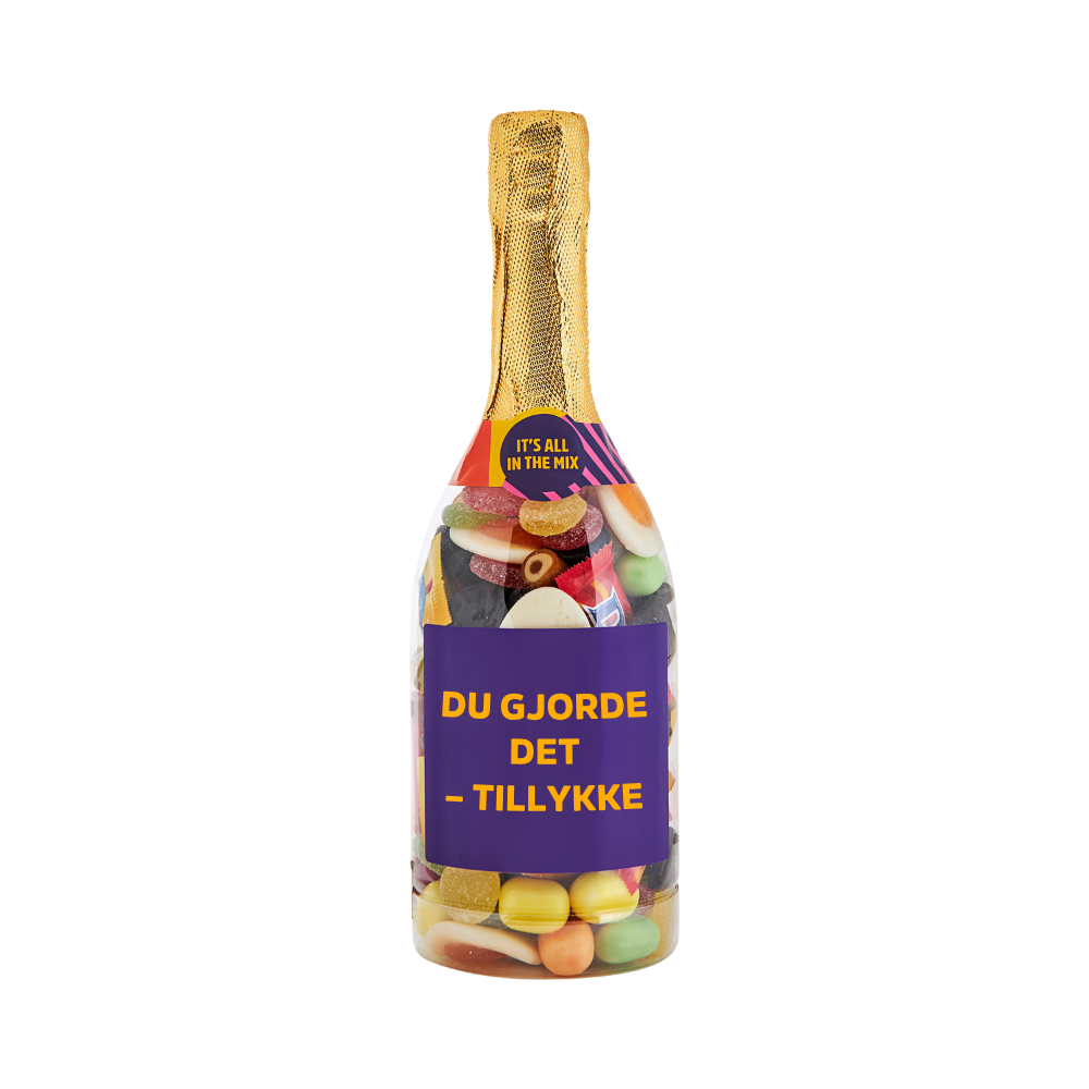 Champagneflaske fyldt med slik og lilla etiket med teksten "Du gjorde det – tillykke" – sød gave fra SlikEkspressen.