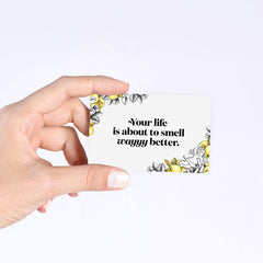 A hand holds a Poo~Pourri Gift Card from ~Pourri with floral and lemon designs, reading Your life is about to smell wayyy better, making it the perfect instant gift to ensure their world always smells fresh.